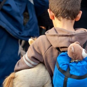 Flüchtlingskind mit Teddy im Rucksack